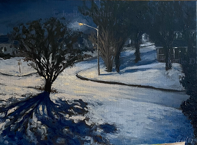 a snowy street at night under an amber street lamp. Trees cast blue shadoes